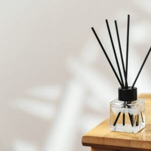 A reed diffuser with black sticks on a wooden surface creating soft shadows.