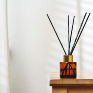 A reed diffuser on a wooden surface with sunlight casting shadows.